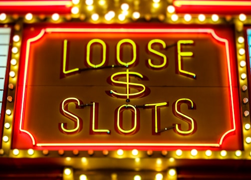 Bright neon lights display the words 'Loose Slots' with a dollar sign in the center. The sign is outlined with bulbs, creating a vibrant and flashy effect typical of a casino or entertainment venue.