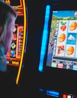 A person is closely observing a digital slot machine with colorful fruit symbols, bars, and a bell. The slot machine screen displays symbols like oranges, plums, cherries, and clouds. The background is dimly lit, creating a focused and somewhat intense atmosphere.